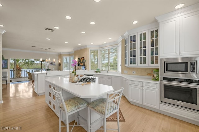 kitchen featuring visible vents, a peninsula, glass insert cabinets, appliances with stainless steel finishes, and a center island