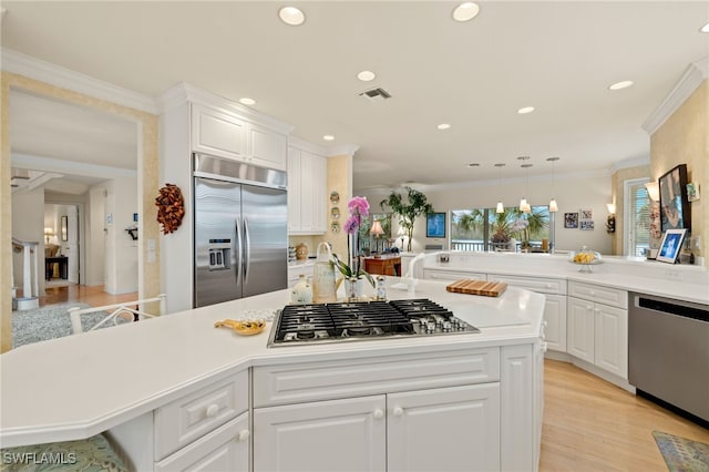 kitchen featuring ornamental molding, appliances with stainless steel finishes, a kitchen breakfast bar, pendant lighting, and white cabinets