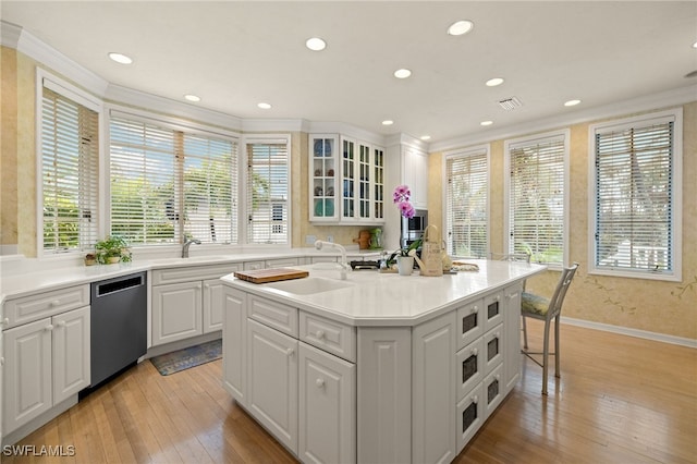 kitchen with white cabinetry, an island with sink, sink, dishwashing machine, and light wood-type flooring