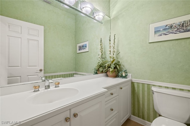 bathroom with a wainscoted wall, toilet, vanity, and wallpapered walls