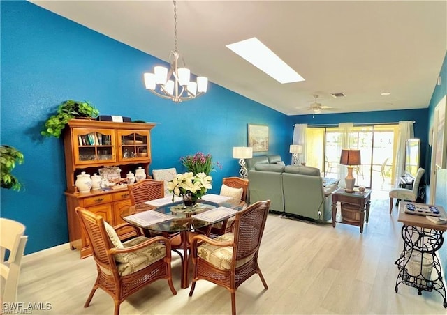 dining space with vaulted ceiling with skylight, ceiling fan with notable chandelier, and light hardwood / wood-style flooring