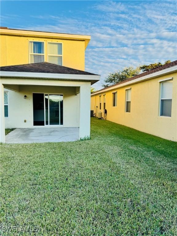 rear view of property with a yard, a patio, and central air condition unit