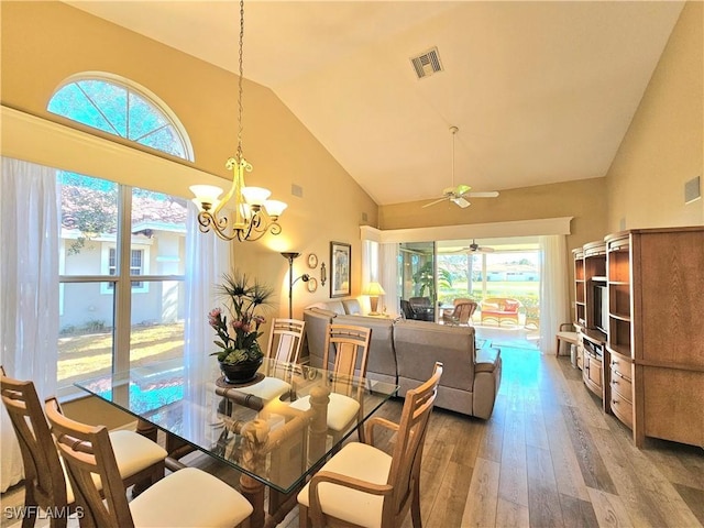 dining area with wood-type flooring, ceiling fan with notable chandelier, and high vaulted ceiling