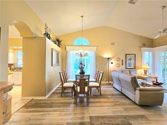 dining space featuring high vaulted ceiling, light wood-type flooring, sink, and an inviting chandelier