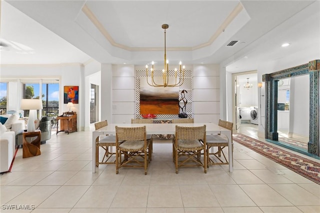 dining room featuring crown molding, a tray ceiling, light tile patterned flooring, washer / dryer, and a chandelier