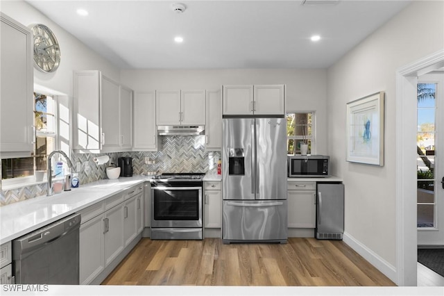 kitchen with white cabinetry, sink, backsplash, light hardwood / wood-style floors, and stainless steel appliances