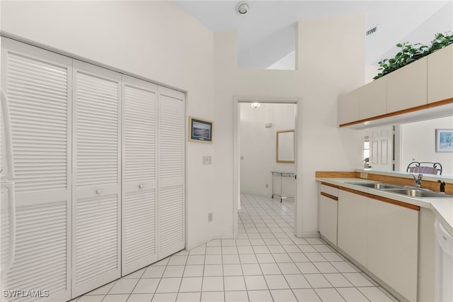 kitchen with white cabinetry, sink, light tile patterned floors, and a towering ceiling