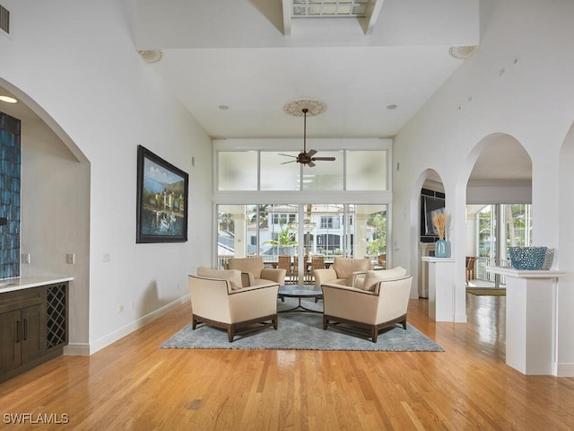 living room featuring a high ceiling, ceiling fan, and light wood-type flooring