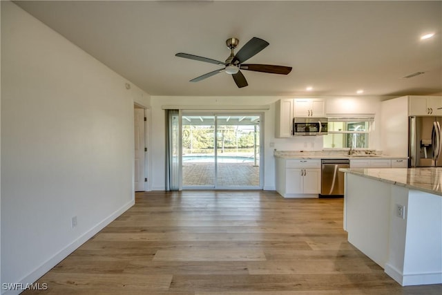 kitchen with stainless steel appliances, white cabinetry, light stone countertops, and light wood-type flooring