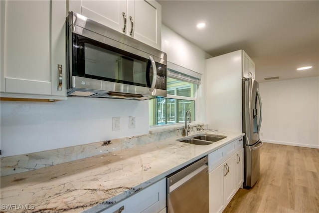 kitchen featuring stainless steel appliances, light stone countertops, sink, and white cabinets