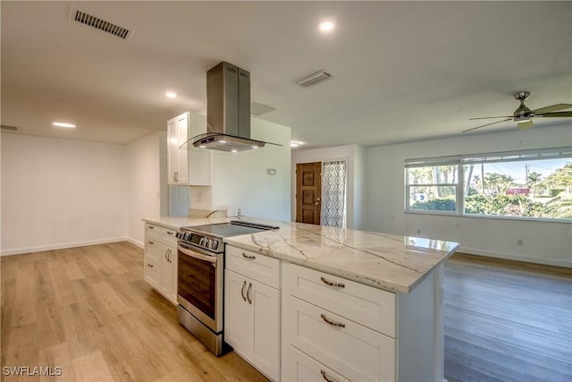 kitchen with stainless steel electric range oven, white cabinetry, island exhaust hood, light stone countertops, and light wood-type flooring