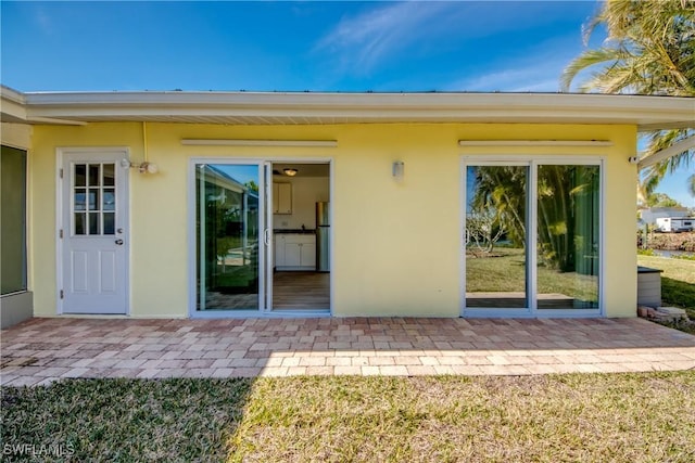 view of exterior entry with a lawn and a patio area