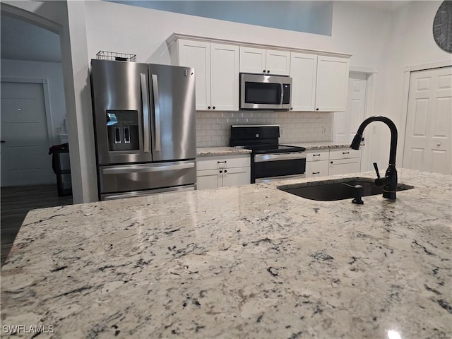 kitchen with appliances with stainless steel finishes, light stone countertops, sink, and white cabinets