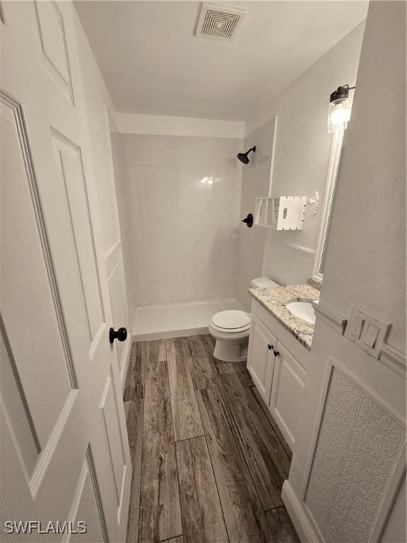 bathroom featuring wood-type flooring, tiled shower, vanity, and toilet