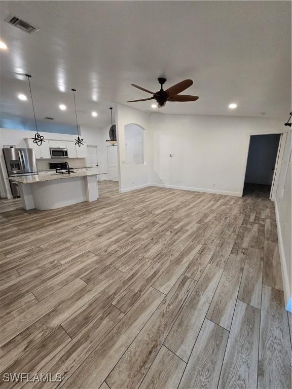 unfurnished living room with ceiling fan, sink, and light wood-type flooring