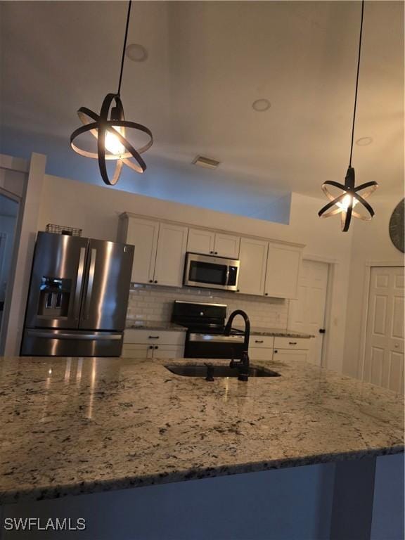 kitchen featuring sink, pendant lighting, stainless steel appliances, light stone countertops, and white cabinets