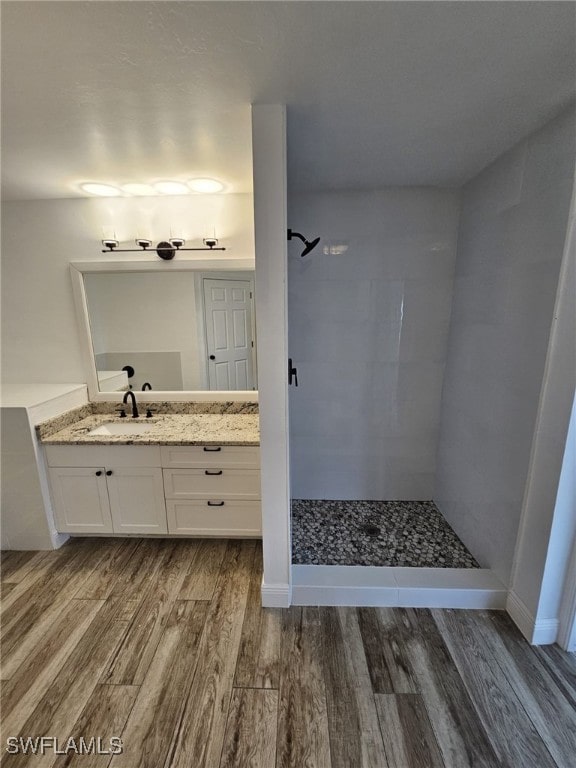 bathroom with wood-type flooring, tiled shower, and vanity