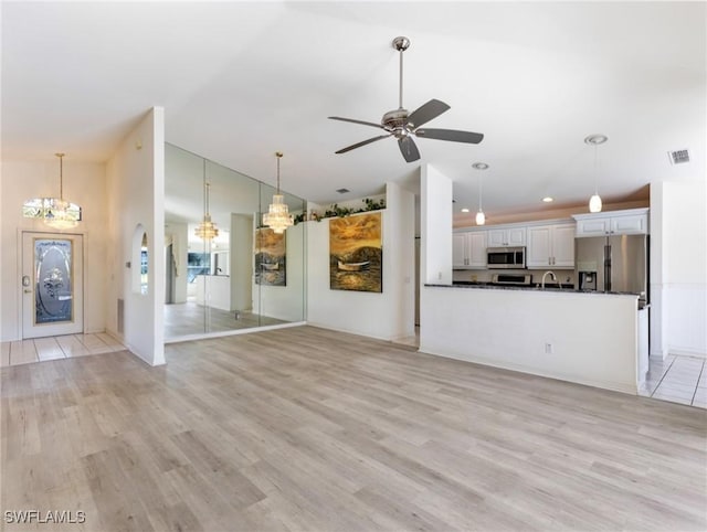 unfurnished living room with vaulted ceiling, ceiling fan with notable chandelier, and light hardwood / wood-style flooring