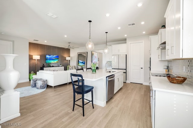 kitchen with white cabinetry, hanging light fixtures, a kitchen island with sink, stainless steel dishwasher, and light hardwood / wood-style floors