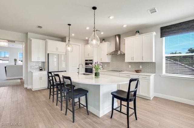 kitchen featuring black electric stovetop, wall chimney range hood, white cabinets, and an island with sink