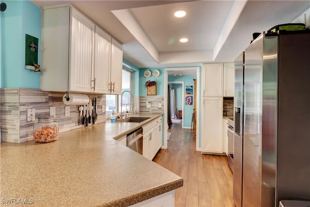 kitchen featuring appliances with stainless steel finishes, sink, white cabinets, decorative backsplash, and a tray ceiling