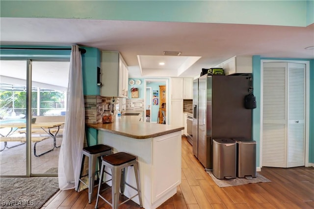 kitchen with white cabinetry, stainless steel fridge with ice dispenser, light hardwood / wood-style flooring, kitchen peninsula, and backsplash