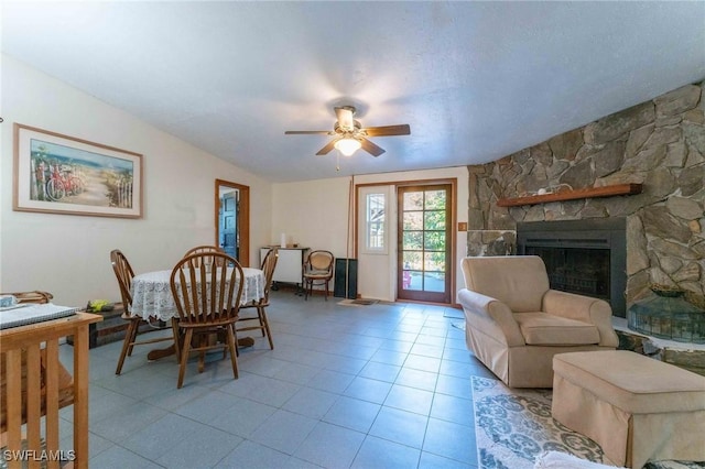 tiled dining room with a stone fireplace, vaulted ceiling, and ceiling fan