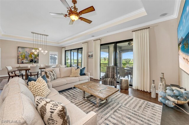 living room featuring hardwood / wood-style flooring, ceiling fan, ornamental molding, and a raised ceiling