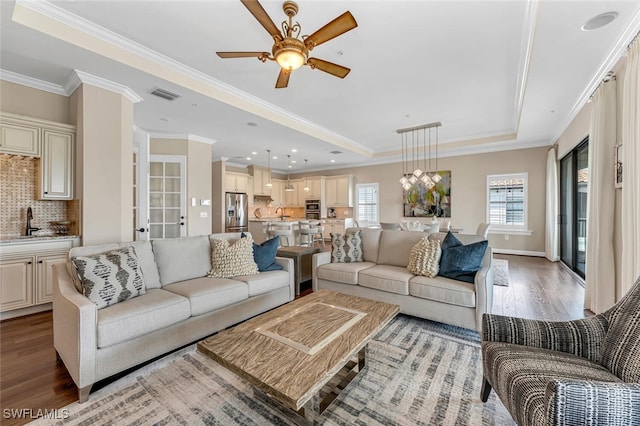 living room with crown molding, sink, light hardwood / wood-style floors, and a tray ceiling