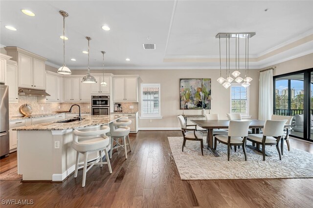 kitchen featuring sink, a kitchen breakfast bar, pendant lighting, light stone countertops, and a kitchen island with sink