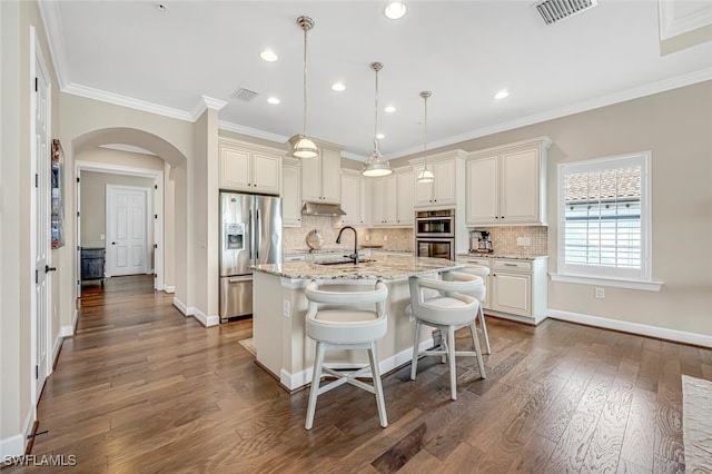 kitchen featuring sink, appliances with stainless steel finishes, hanging light fixtures, light stone countertops, and a center island with sink