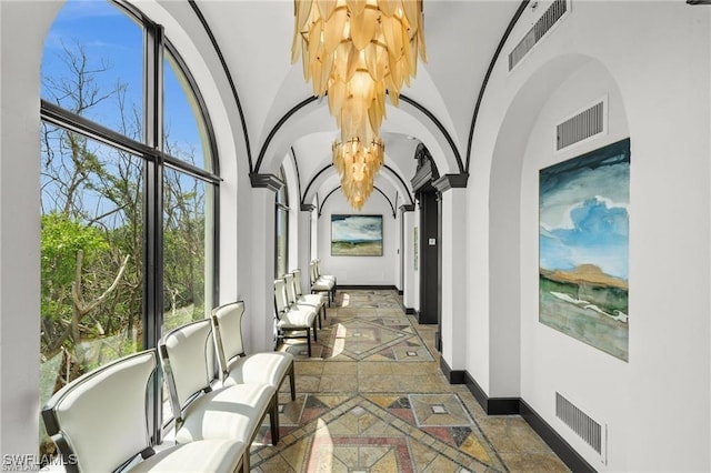 hallway with an inviting chandelier, vaulted ceiling, and decorative columns