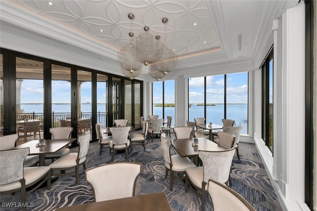 sunroom with a tray ceiling, french doors, and a water view