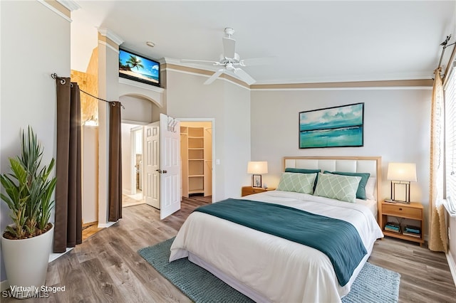 bedroom featuring crown molding, hardwood / wood-style flooring, ceiling fan, vaulted ceiling, and a walk in closet