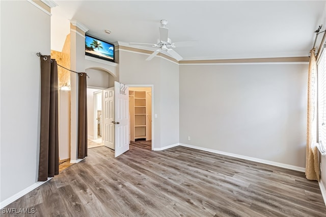 unfurnished bedroom featuring a walk in closet, wood-type flooring, ornamental molding, and ceiling fan