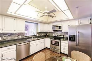 kitchen featuring ceiling fan, appliances with stainless steel finishes, dark hardwood / wood-style floors, white cabinets, and decorative backsplash