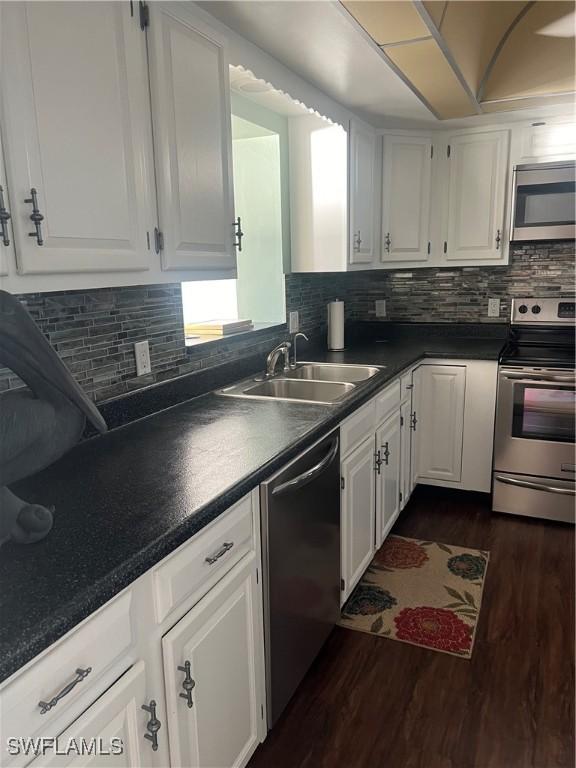 kitchen with sink, dark wood-type flooring, appliances with stainless steel finishes, white cabinetry, and tasteful backsplash