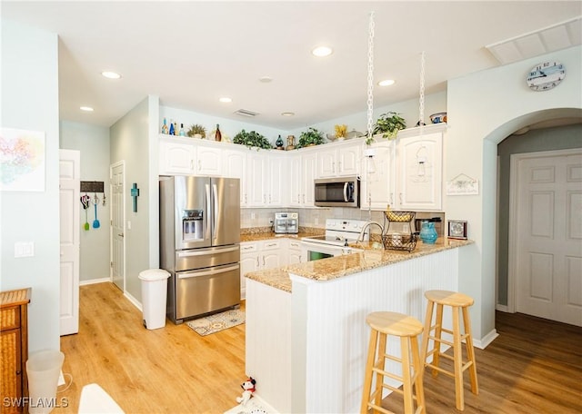 kitchen with light hardwood / wood-style flooring, white cabinetry, stainless steel appliances, light stone countertops, and kitchen peninsula