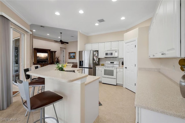 kitchen featuring tasteful backsplash, crown molding, a kitchen breakfast bar, white appliances, and white cabinets