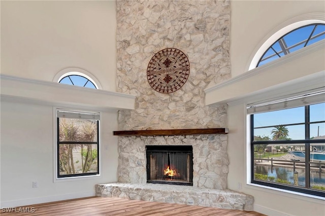 unfurnished living room featuring a high ceiling, a water view, hardwood / wood-style floors, and a fireplace