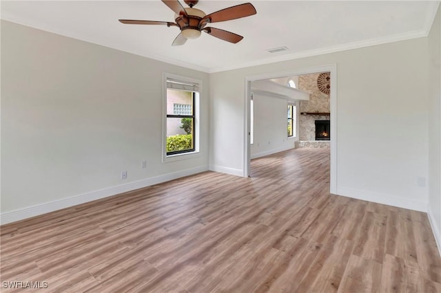 unfurnished room with a stone fireplace, ornamental molding, and light hardwood / wood-style floors