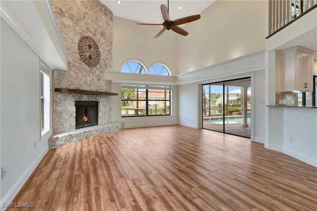 unfurnished living room with ceiling fan, a towering ceiling, a fireplace, and light hardwood / wood-style flooring