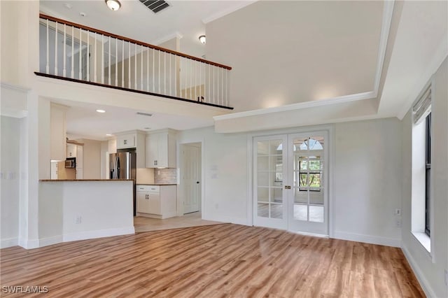 unfurnished living room with a high ceiling, ornamental molding, light hardwood / wood-style floors, and french doors