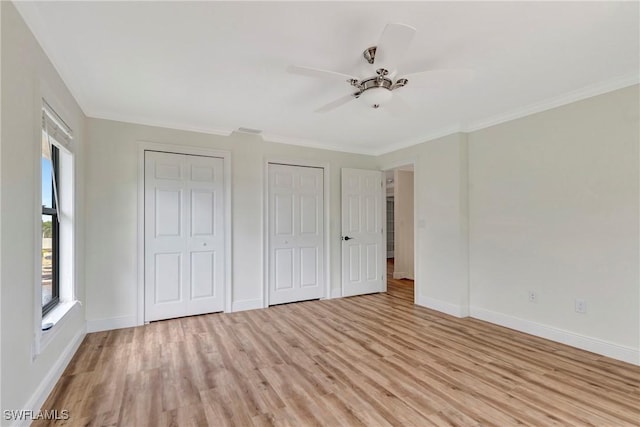 unfurnished bedroom featuring crown molding, multiple closets, and light wood-type flooring