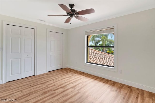 unfurnished bedroom featuring ornamental molding, two closets, ceiling fan, and light hardwood / wood-style floors