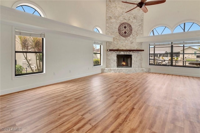 unfurnished living room with a high ceiling, ceiling fan, a fireplace, and light hardwood / wood-style flooring