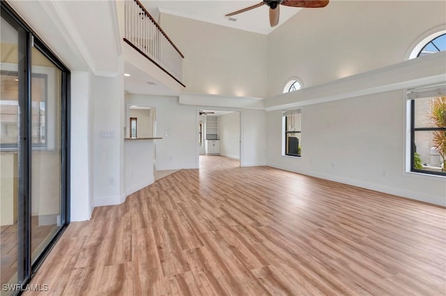 unfurnished living room featuring a high ceiling, crown molding, light wood-type flooring, and ceiling fan