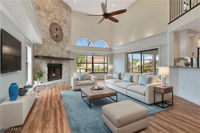 living room featuring ceiling fan, a towering ceiling, a fireplace, and hardwood / wood-style floors