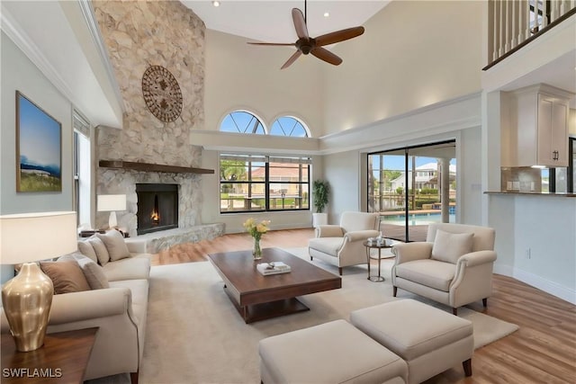 living room featuring ceiling fan, a towering ceiling, a fireplace, and light hardwood / wood-style floors