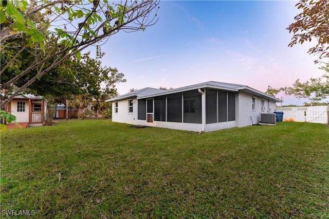 back of house at dusk featuring a sunroom, fence, a lawn, and central AC unit